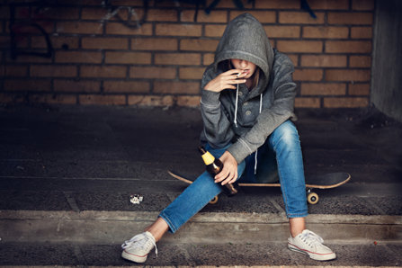 Teenager girl sitting on a skateboard, drinking and smoking.