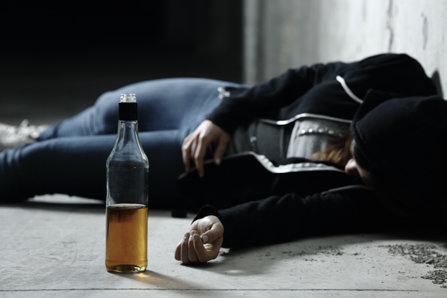 Drunk teenager is laying with alcohol on a floor